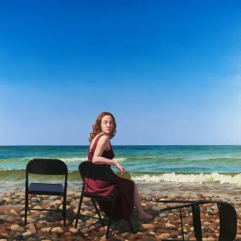 A woman in a maroon dress sits on a black folding chair on a rocky beach, looking over her shoulder. Two more black chairs are nearby, one upright and one toppled, with blue sky and calm sea in the background.