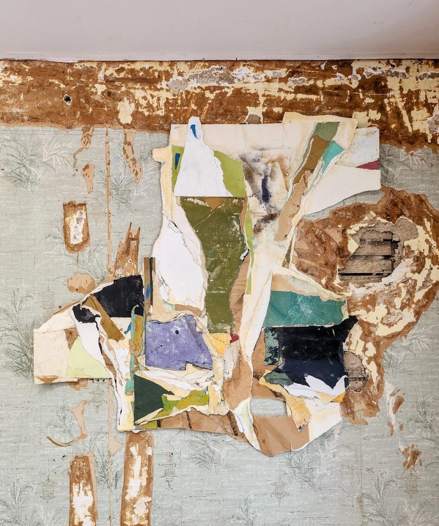 Torn and layered wallpaper reveals various colors and patterns beneath, exposing plaster and wooden lath on a damaged wall. The top of the wall has extensive peeling and water damage.