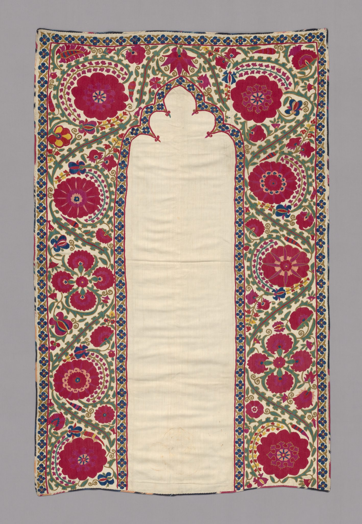 A rectangular textile with a central plain white panel framed by colorful floral embroidery in red, pink, green, and blue on a beige background, featuring a pointed arch shape at the top of the panel.